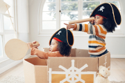 Pirate, box and playing with children in living room for bonding, imagine and creative. Happy, youth and siblings with girls sailing in cardboard ship in family home for relax, fantasy and games