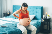 Pregnant woman feeling pain while sitting on bed