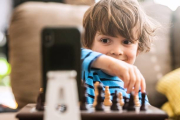 Niño jugando al ajedrez y mirando el móvil