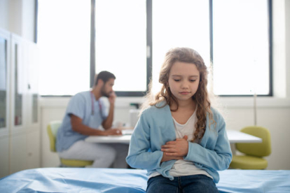 Little girl with pain in belly sitting in doctors office at hospital