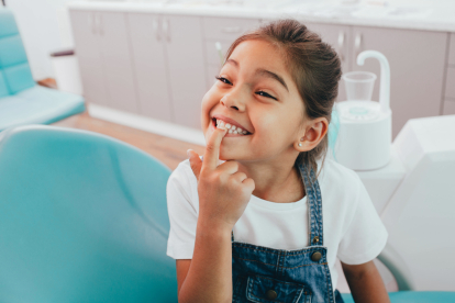 Mixed race little patient showing her perfect toothy smile while sitting dentists chair