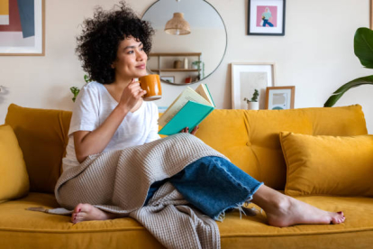 Madre leyendo libro en el sofá con una taza de té o café